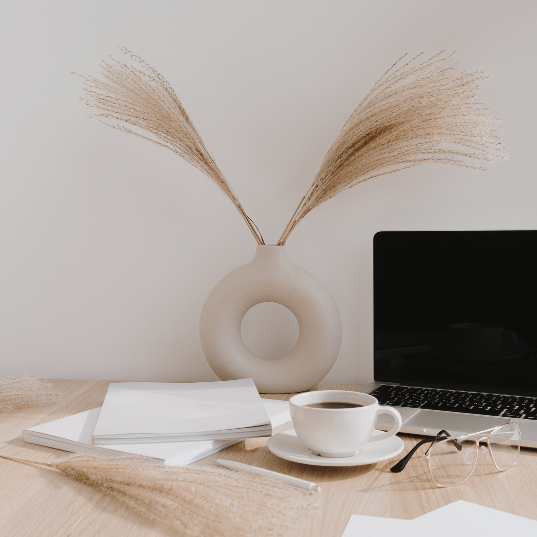 Vase with dried stems sitting on a desk with a desktoop computer, coffee cup, and notepaper