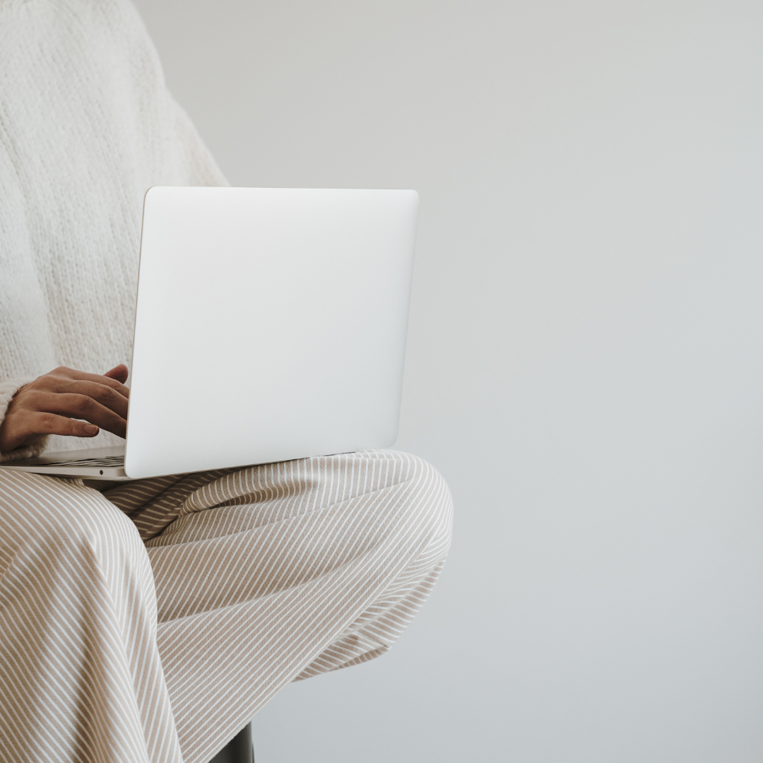 Woman sits on a stool with her laptop while writing a wedding blog post