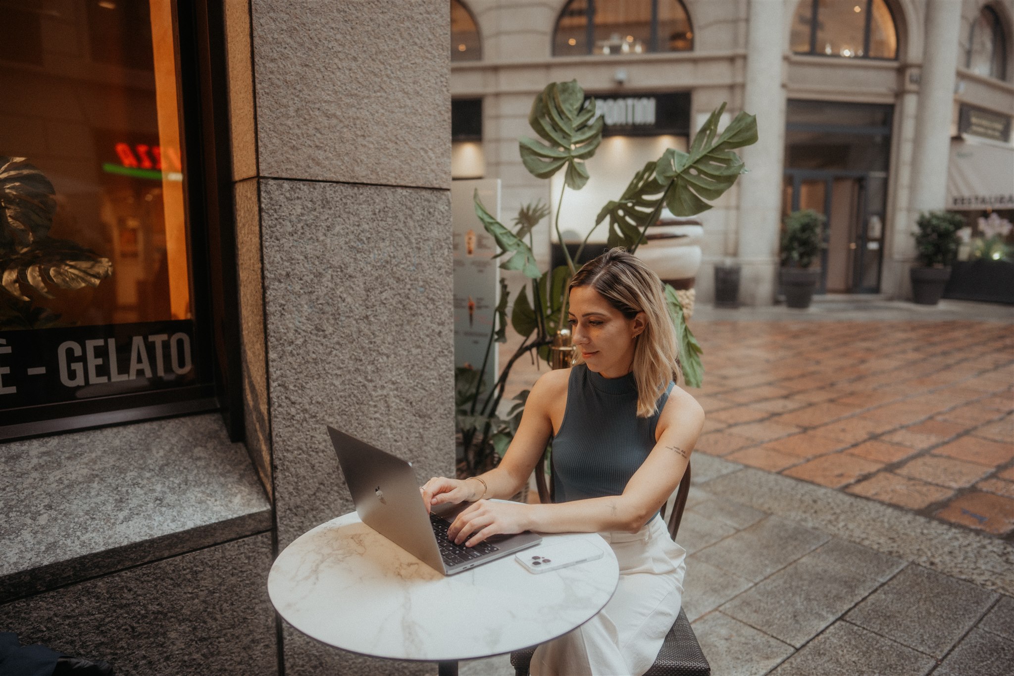 Woman sits at an outdoor bistro table working on her laptop. 
