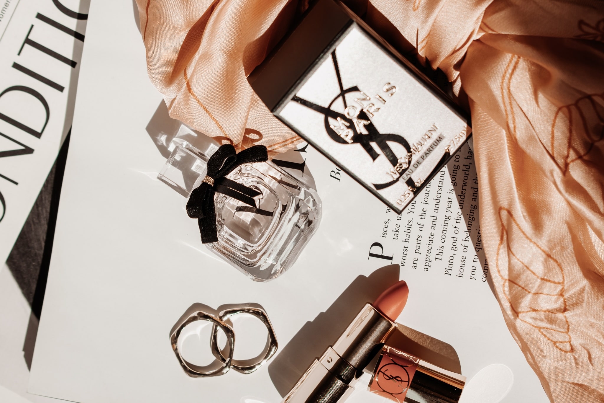 Detail flatlay with YSL perfume and makeup on top of a printed book and magazine