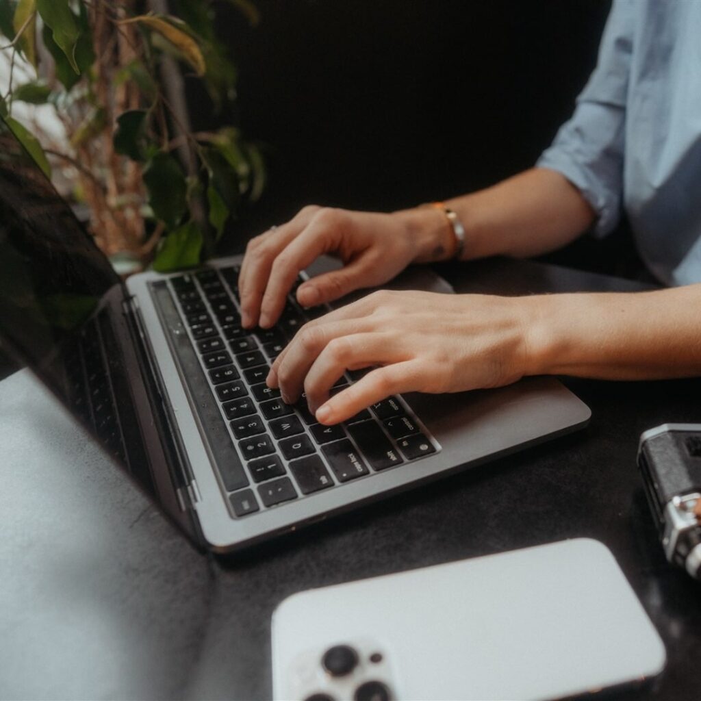 Woman types on a macbook pro computer about how to write an interesting blog post.