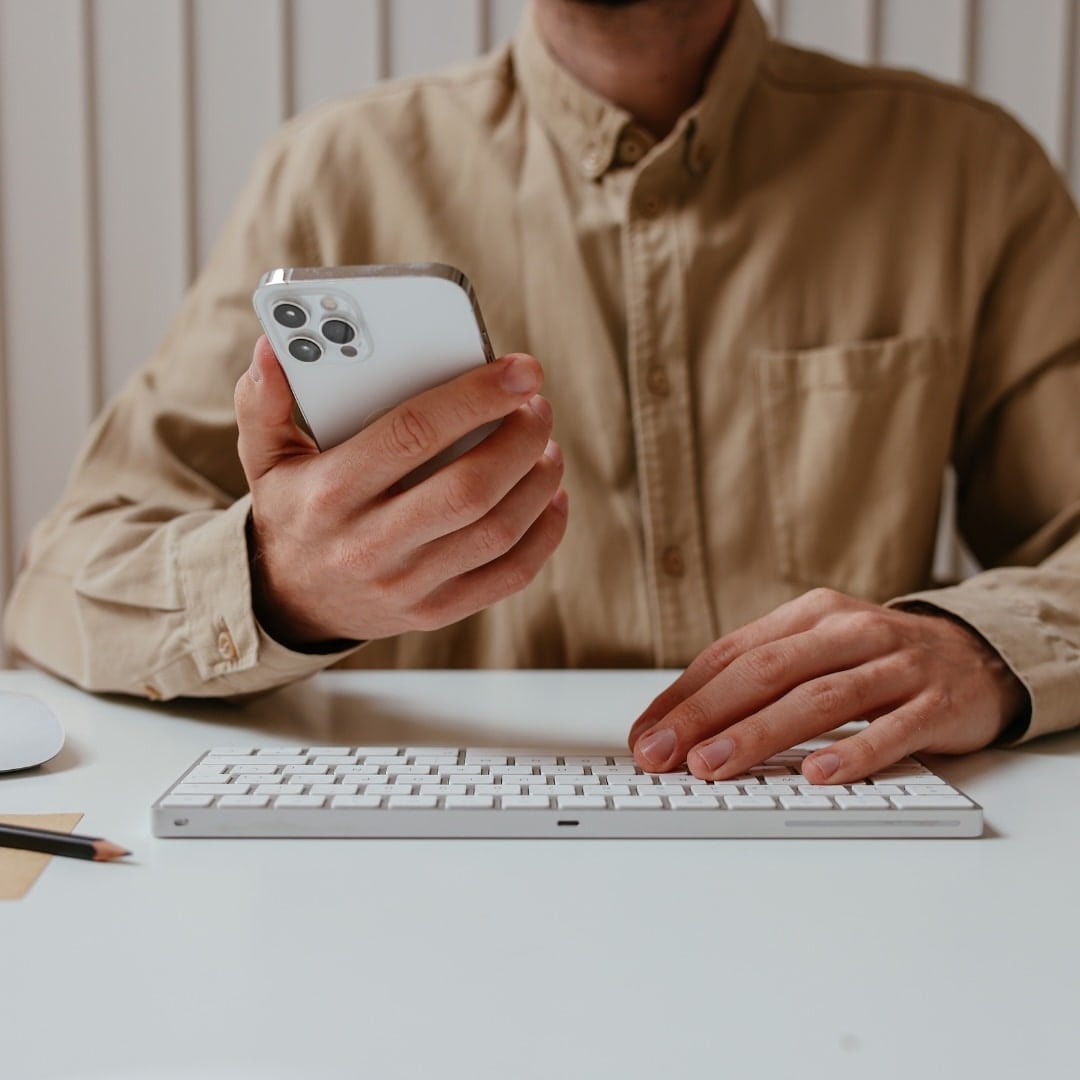Man sits at a keyboard holding an iPhone learning how to optimize a Pinterest profile and account.