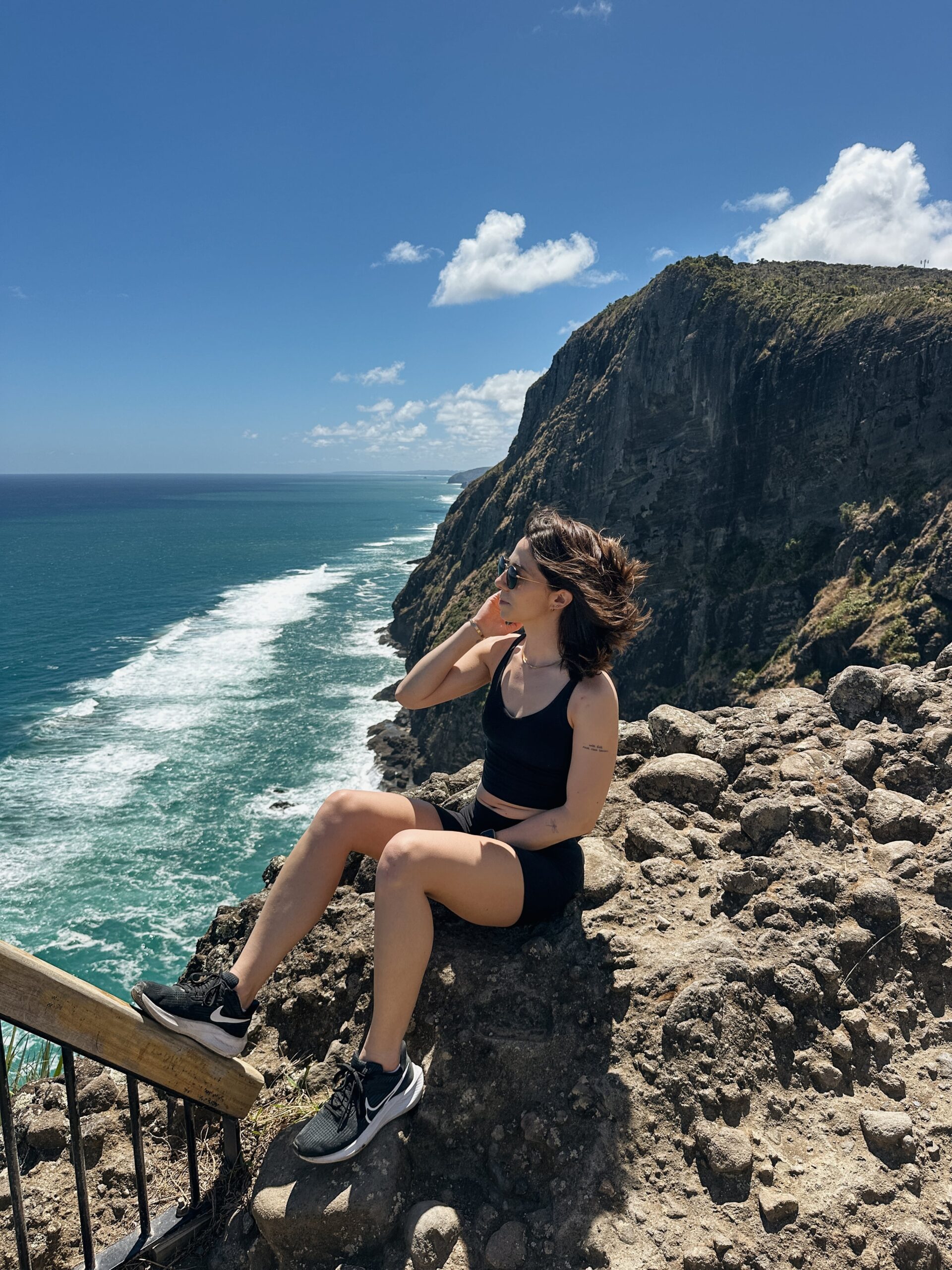 Woman sitting on a cliff overlooking the ocean at a hike in New Zealand.
