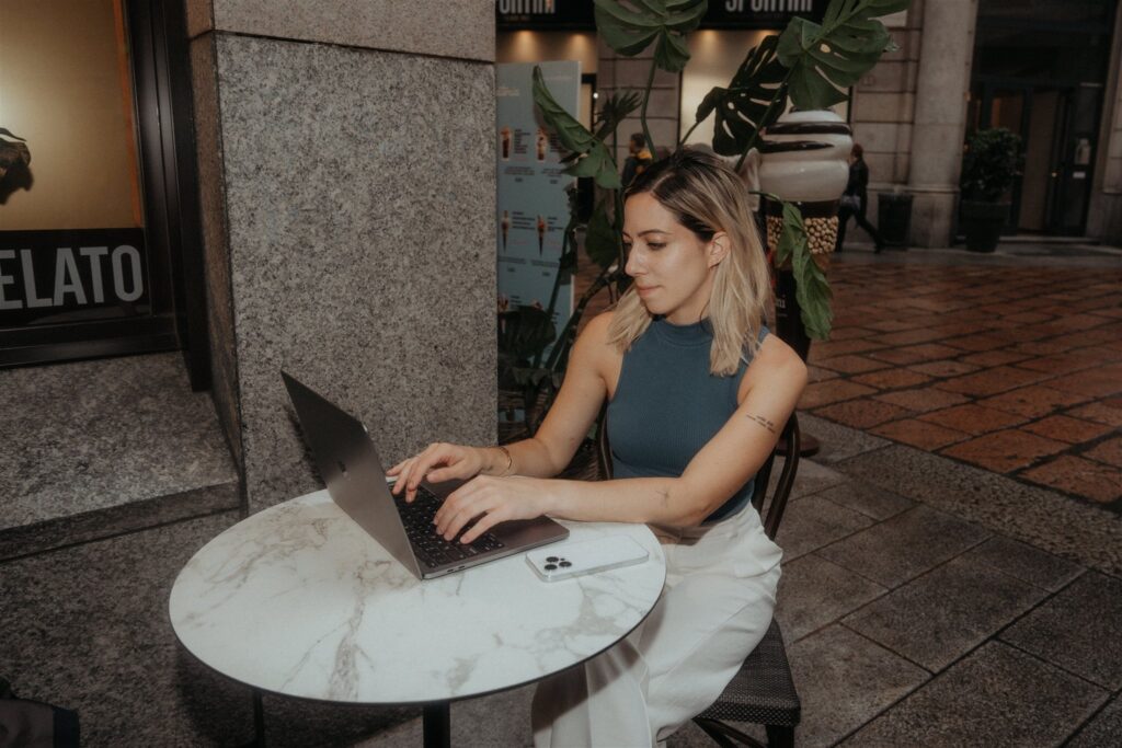 Woman sits at an outdoor cafe in Milan and works on her laptop.