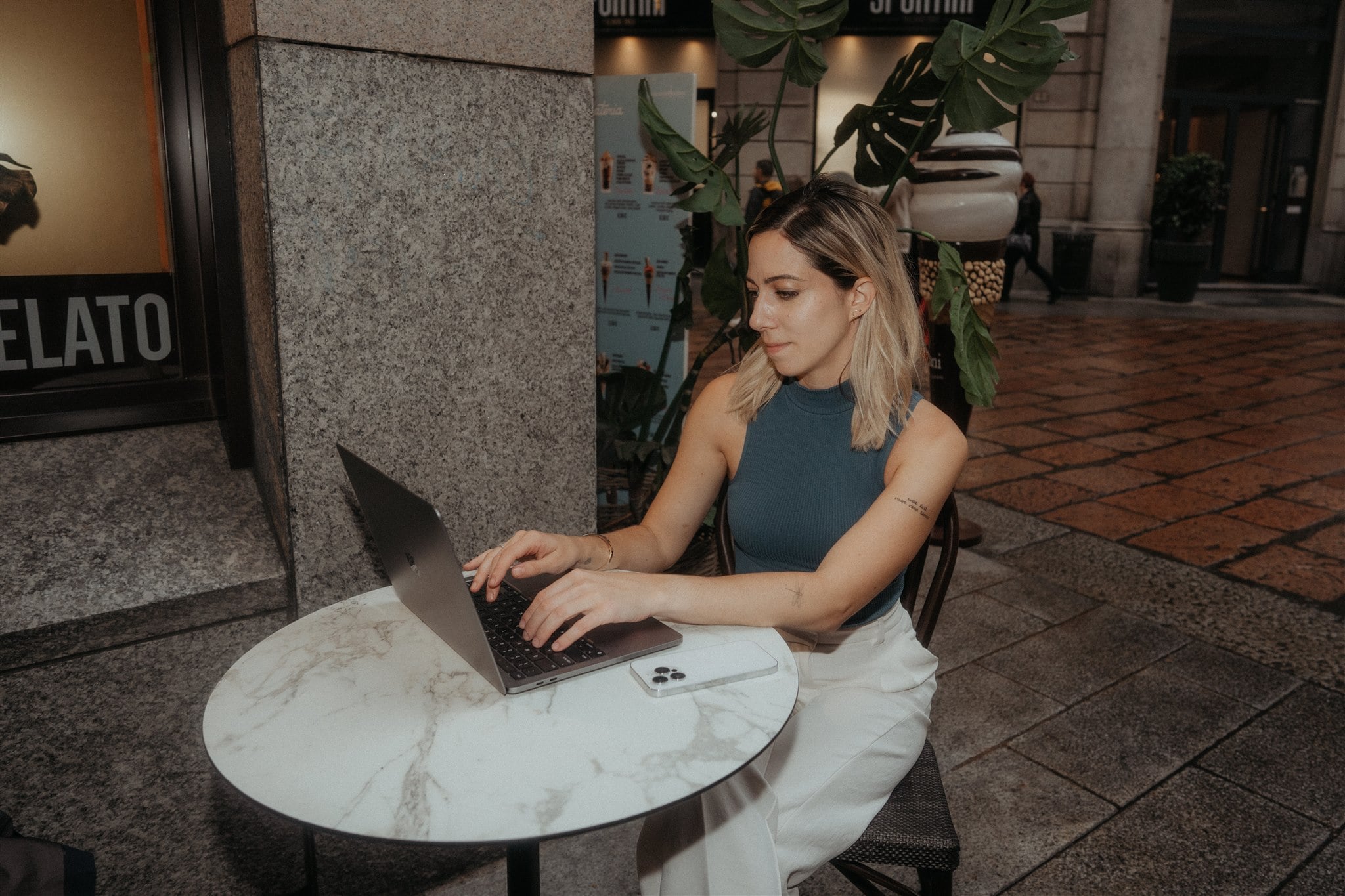 Woman sits at an outdoor cafe in Milan and works on her laptop.
