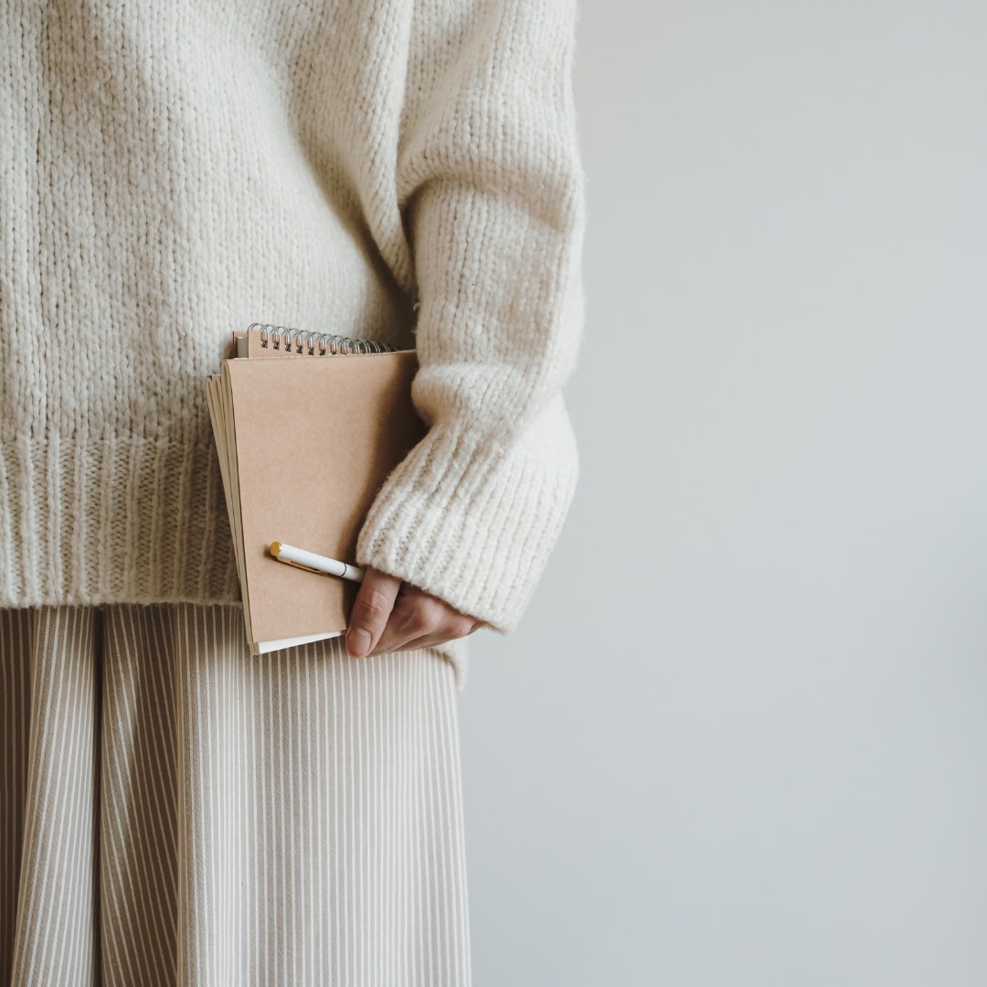 Woman holding a few notebooks and a pen.