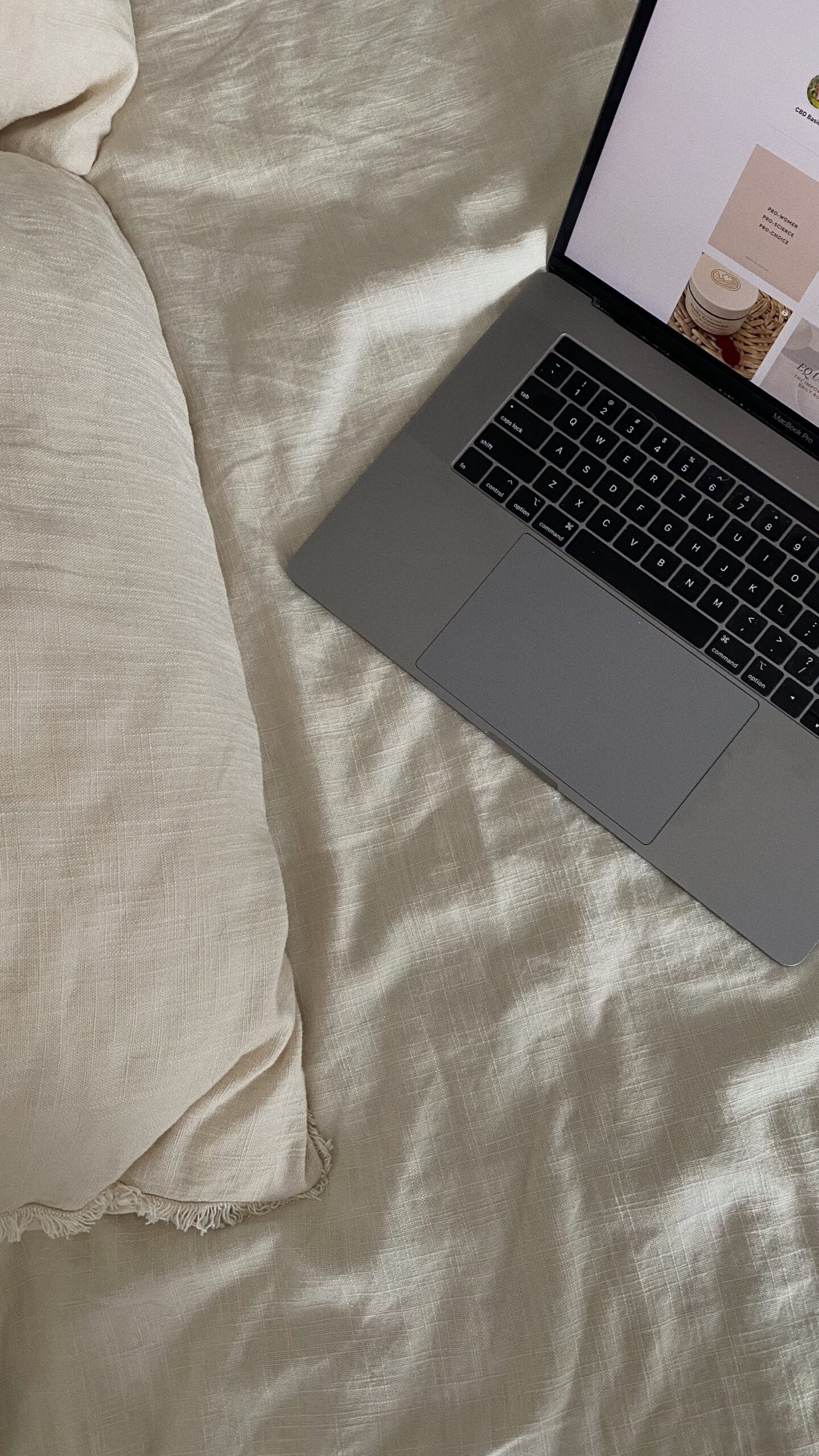 Macbook laptop sits on a linen bedspread.