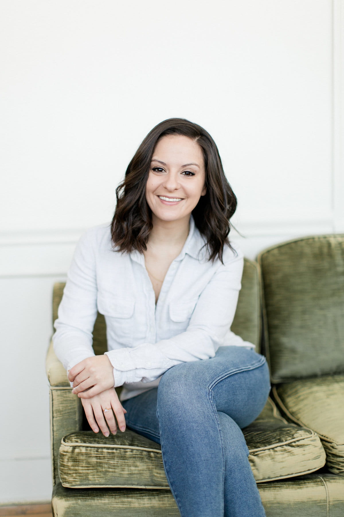 East Coast wedding photographer sits on a green velvet sofa.