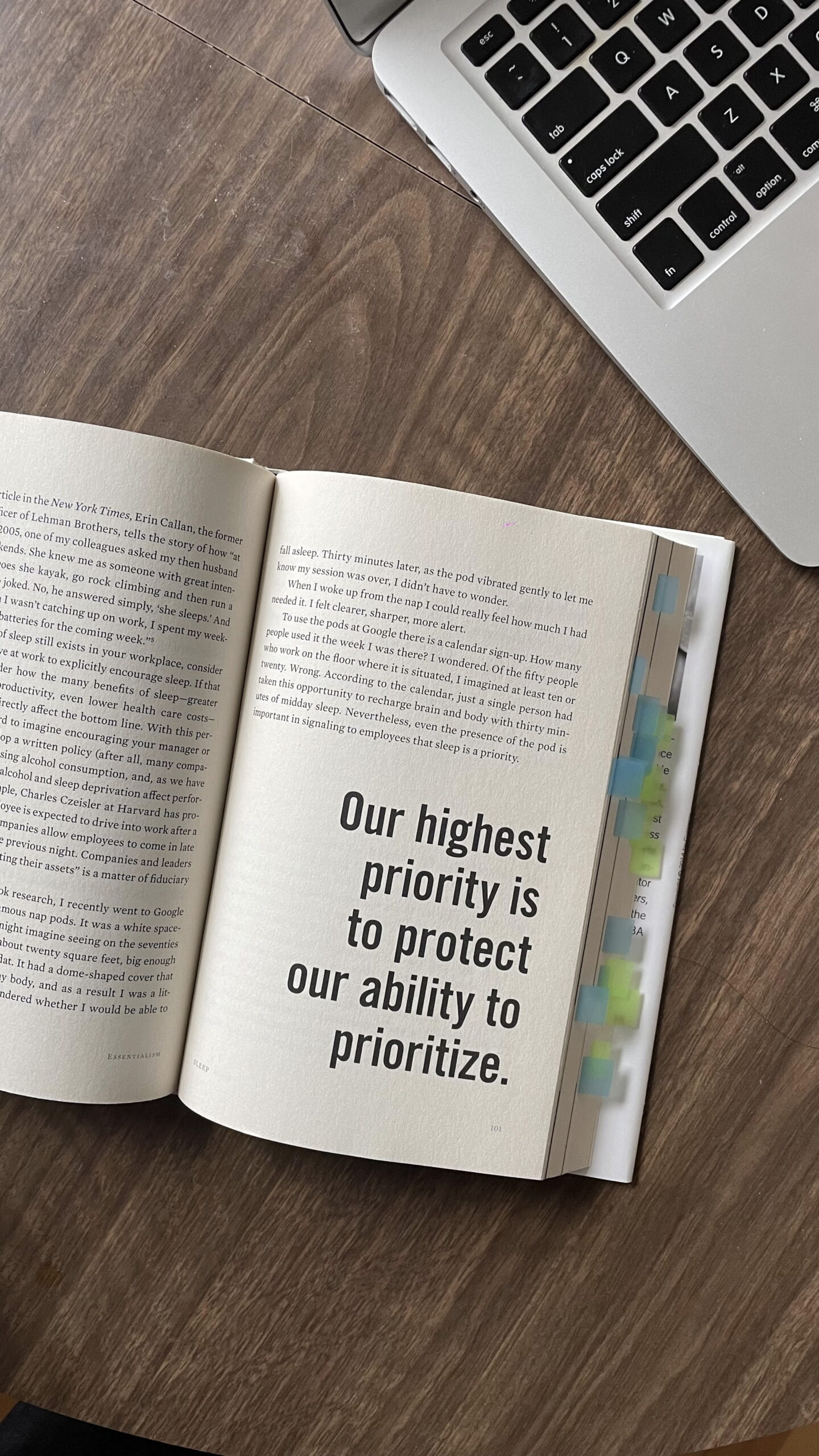 Laptop computer sits on a wood table next to an open book with text "Our highest priority is to protect our ability to prioritize."